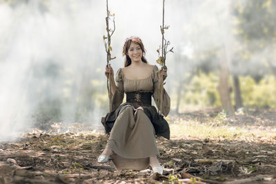 Full length portrait of young woman on swing at field