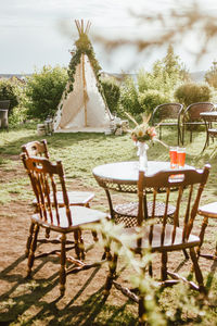 Empty chairs and table by river against sky