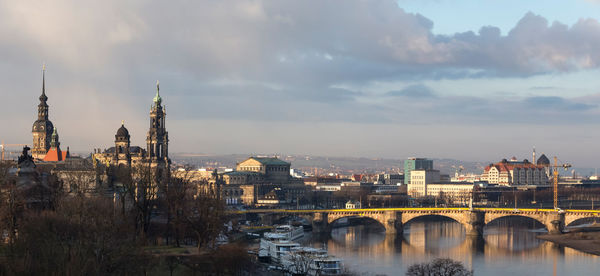 Bridge over river in city against cloudy sky