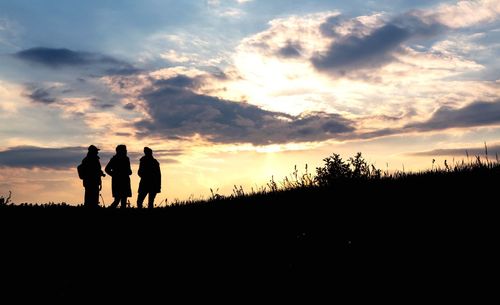 Silhouette people standing on landscape against sky during sunset