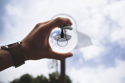 Cropped hand of person holding crystal ball against sky