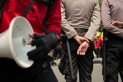 Rear view of police men with hands behind back standing on street in city