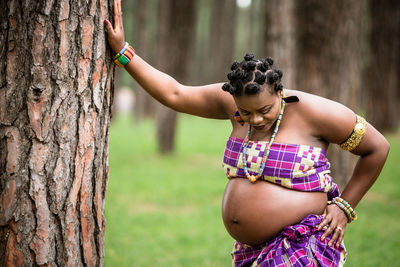 Midsection of woman standing by tree trunk