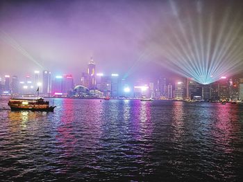 Illuminated buildings by river against sky at night