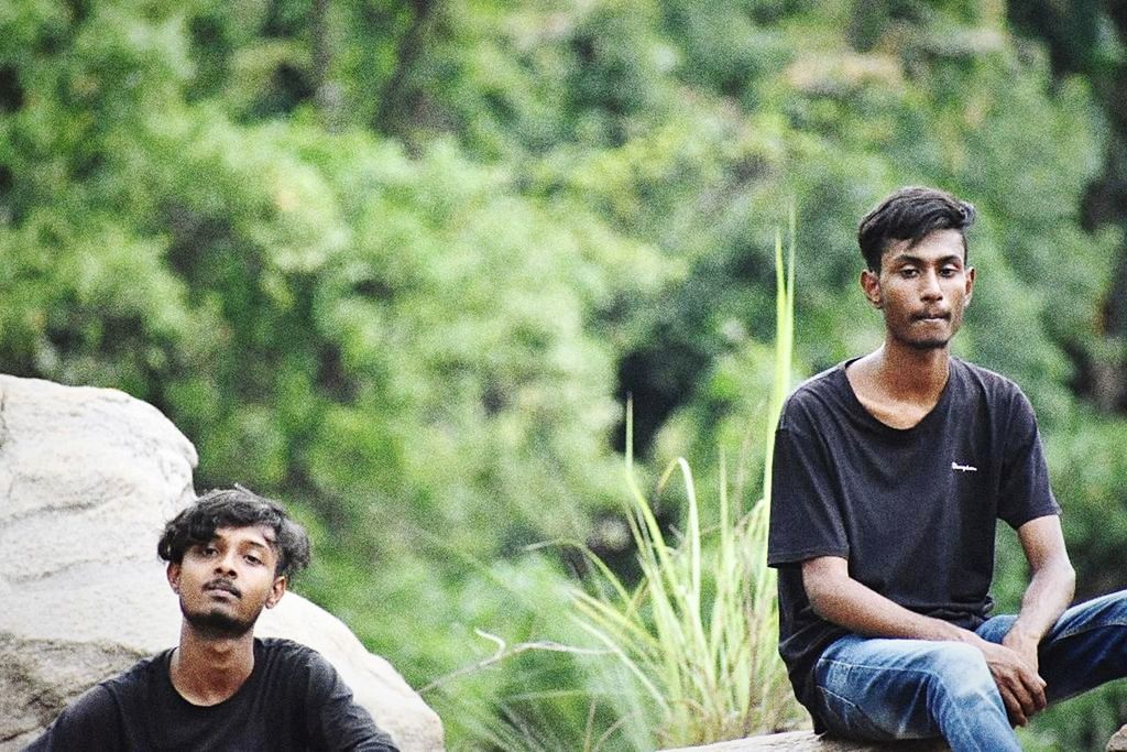 young men, young adult, casual clothing, sitting, focus on foreground, leisure activity, real people, looking, front view, people, men, day, portrait, looking away, lifestyles, nature, contemplation, three quarter length, friendship, plant, outdoors