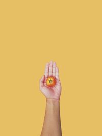 Close-up of person hand holding fruit against yellow background