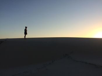 Woman standing on sand against clear sky during sunset