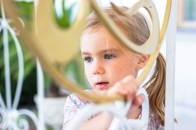 Curious little girl gazing through a beautifully ornate golden fence, captivated by the world beyond