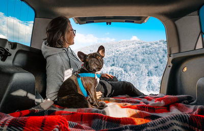 Man and french bulldog dog traveling and sitting in car trunk in winter