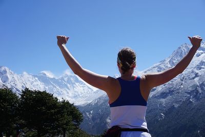 Rear view of woman with arms outstretched standing against mountain 