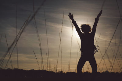 Silhouette carefree woman with arms raised standing on field at sunset