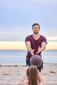 Friends exercising with ball at beach against sky