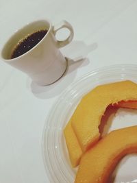 High angle view of coffee cup by fruit in plate on table