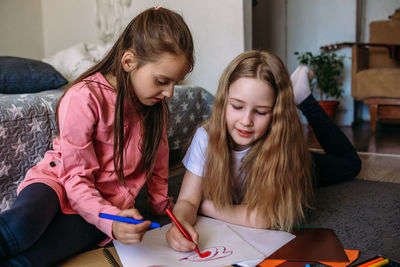 Two girls friends play at home, draw with pencils and felt-tip pens and have fun