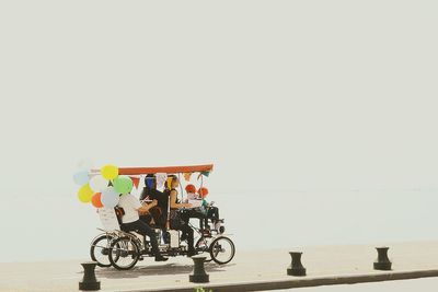 People riding bicycle by sea against sky