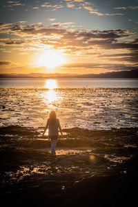 Rear view of woman standing on beach during sunset