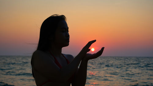 Side view of young woman with arms raised at beach during sunset