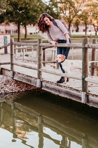 Smiling woman standing with dog on pier by lake