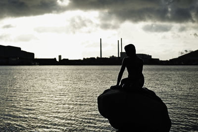 Rear view of silhouette man standing by lake against sky during sunset