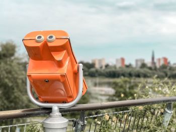 Close-up of coin-operated binoculars by cityscape against sky