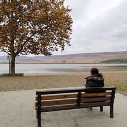 Rear view of woman sitting on bench against lake