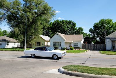 Car on road by trees and buildings against sky