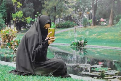 Woman in burka using mobile phone against pond