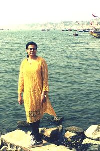 Portrait of young man standing on rock by sea