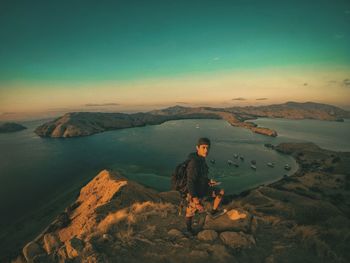 Rear view of man sitting on mountain against sky during sunset