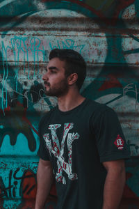 Young man looking away while standing against wall