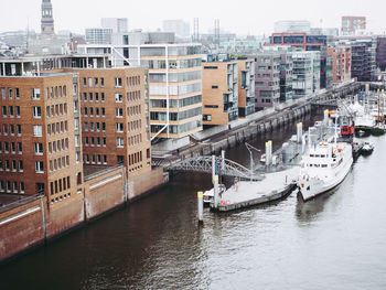 Boats in river by buildings in city against sky