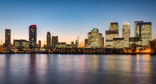 Modern buildings by thames river at canary wharf during sunset in city
