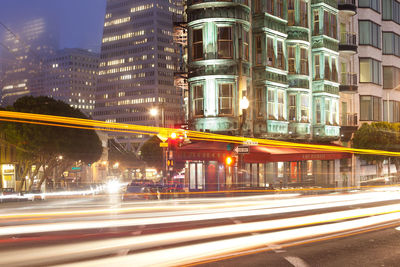 Light trails on road by buildings in city at night