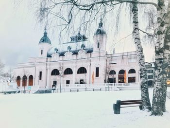 Snow covered built structure by bare trees and building