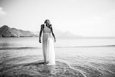 Rear view of woman standing at sea shore against sky