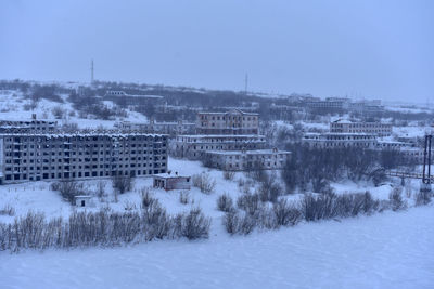 Snow covered field by buildings against sky