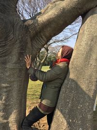 Side view of young woman standing by tree trunks