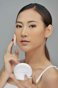 Close-up portrait of beautiful young woman applying compact powder