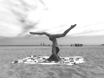 Woman stretching legs at beach against sky