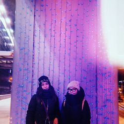 Portrait of young woman standing against illuminated wall during winter