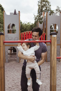 Male toddler with father hanging on monkey bar in playground