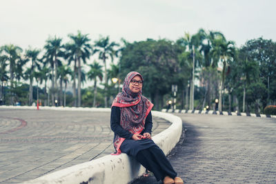 Thoughtful young woman sitting on dividing line at street