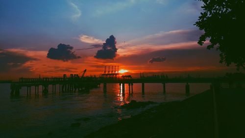 Silhouette pier over sea against orange sky