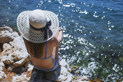 Back view of a woman with hat sitting by the sea