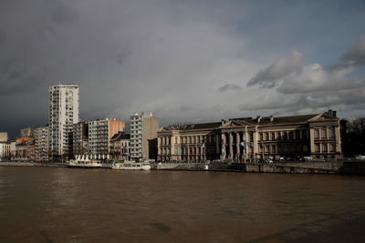 Buildings by river against sky in city