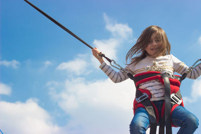 Low angle portrait of girl enjoying bungee jumping against sky