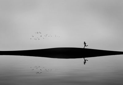 Silhouette woman running on sand dune by reflection in lake against sky