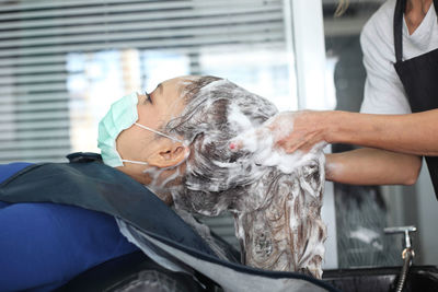 Midsection of hairdresser washing woman hair in salon