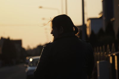 Rear view of silhouette woman standing against sky during sunset