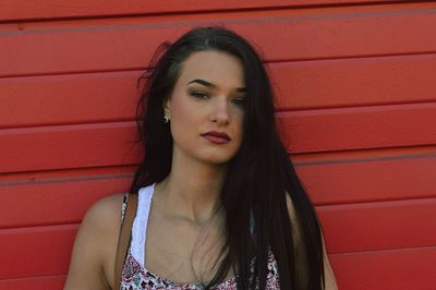 Close-up portrait of beautiful woman standing by red wall